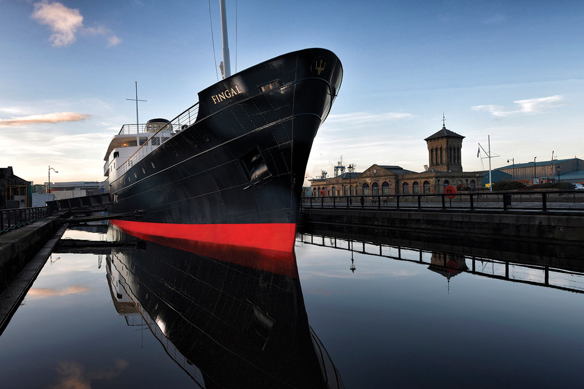 Daytime image of Fingal luxury ship berthed in Leith, Edinburgh, with striking black and red hull reflected in calm harbour water