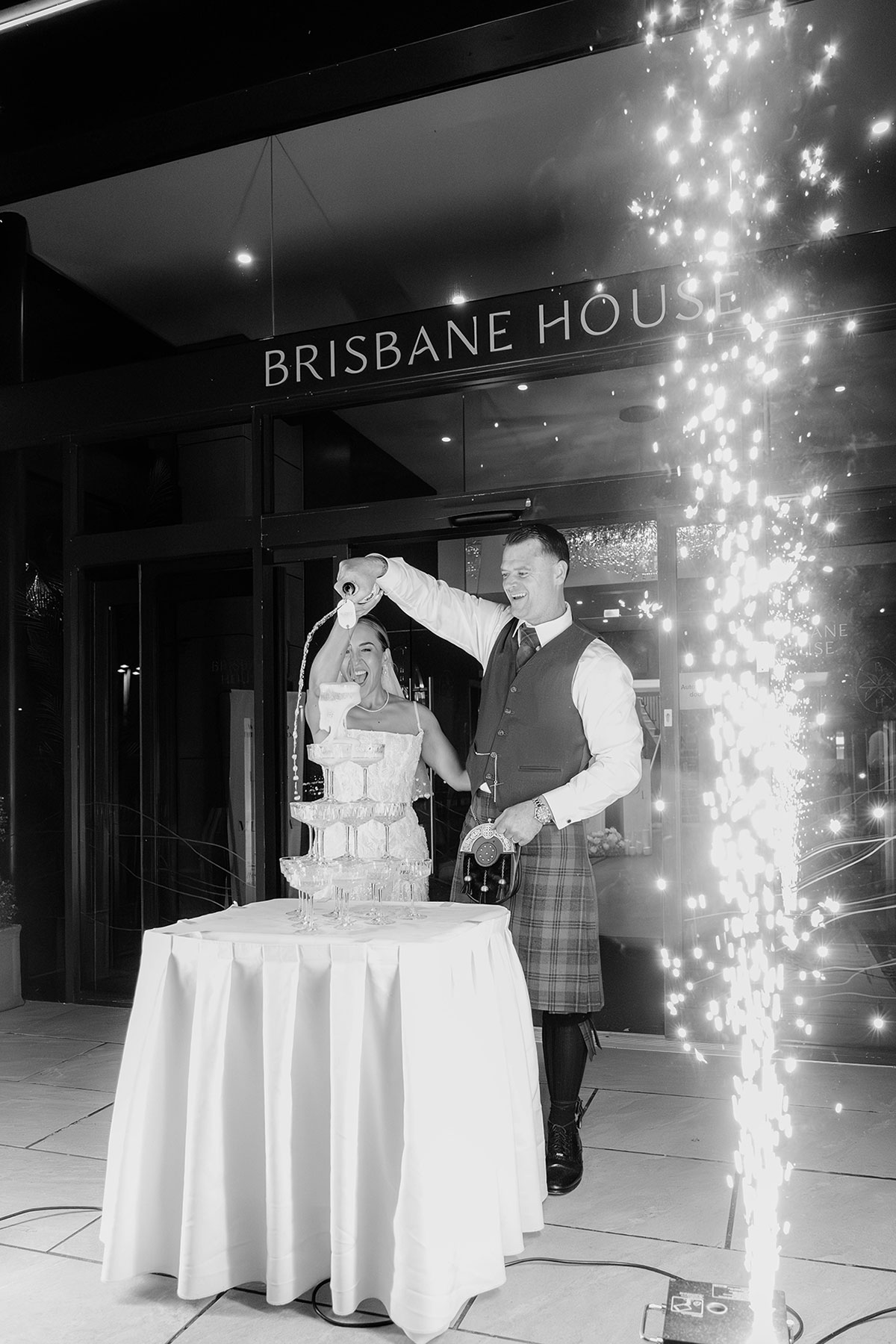 Bride and groom pouring champagne tower with sparklers outside Brisbane House Hotel reception