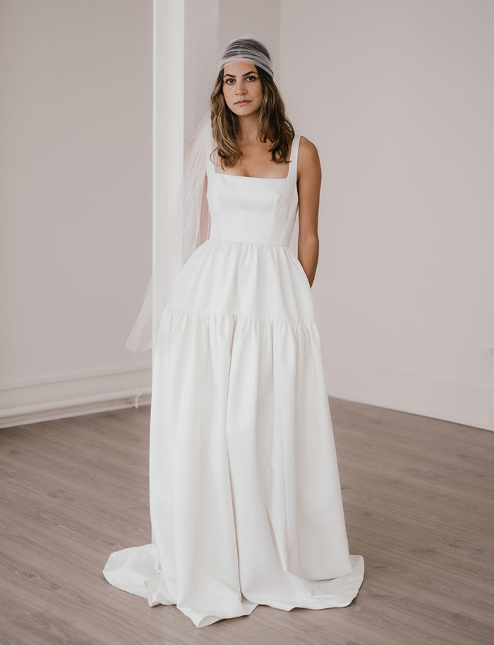 brunette woman wears a white sleeveless tiered full-length dress and a tulle veil wrapped as a headpiece