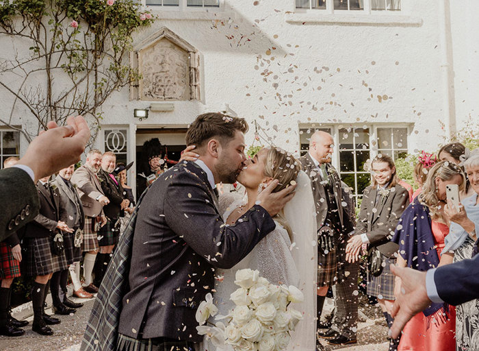 a bride and groom kiss as they are showered in delicate confetti as guests gather around outside Achnagairn Castle