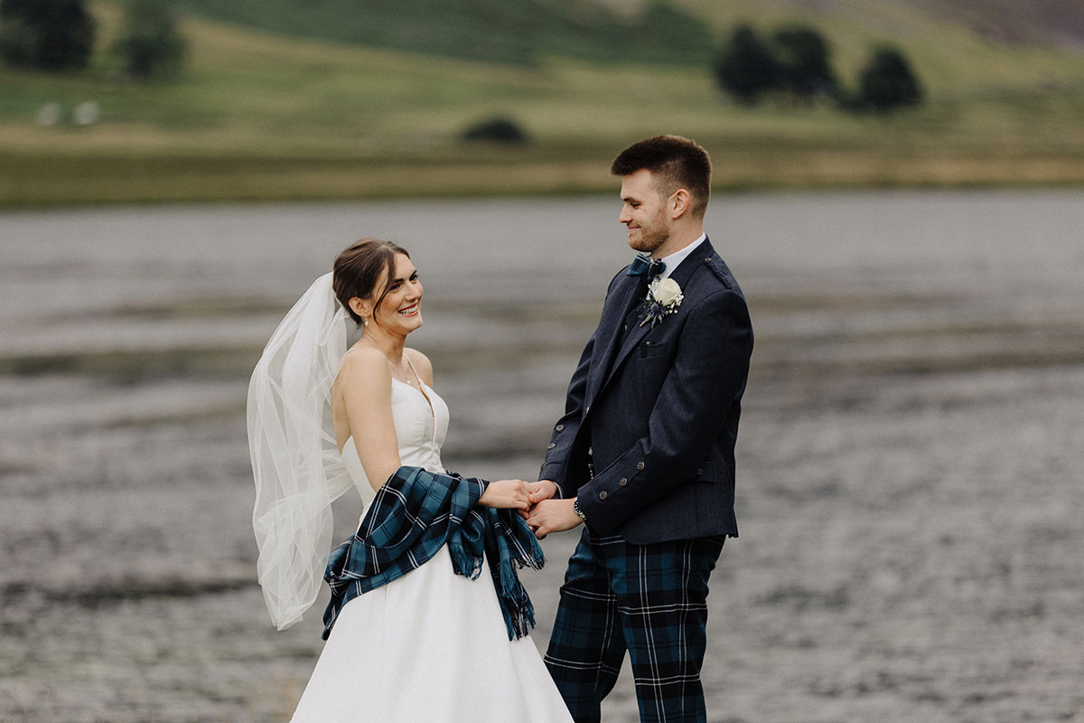Couple holding hands and laughing in front of a loch