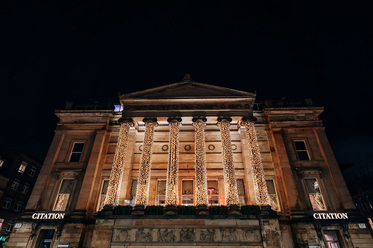 Exterior of Citation Glasgow at nighttime with tall pillars illuminated with fairy lights