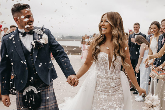 couple happy and smiling as guests throw confetti on them after wedding ceremony 