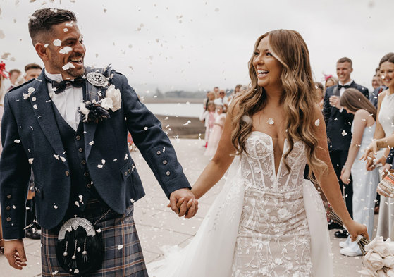 couple happy and smiling as guests throw confetti on them after wedding ceremony 