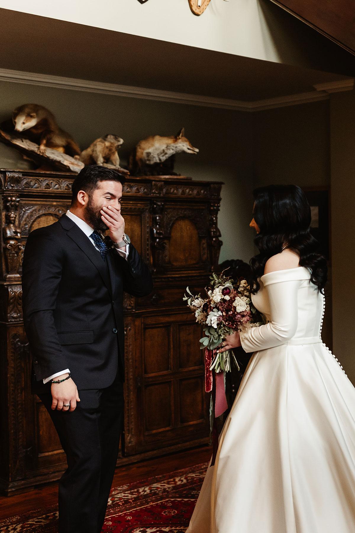 Emotional groom covering his mouth as he sees the bride in her off-the-shoulder gown for the first time, bouquet in hand 