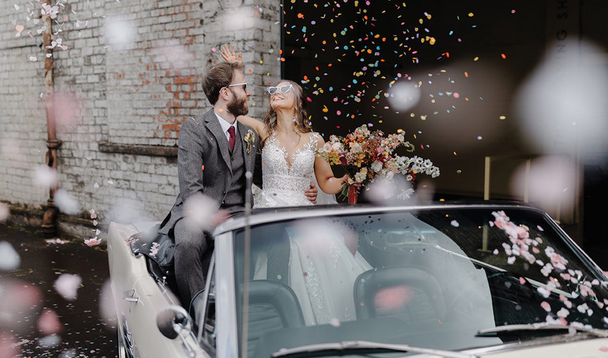 A bride and groom in a car with confetti falling