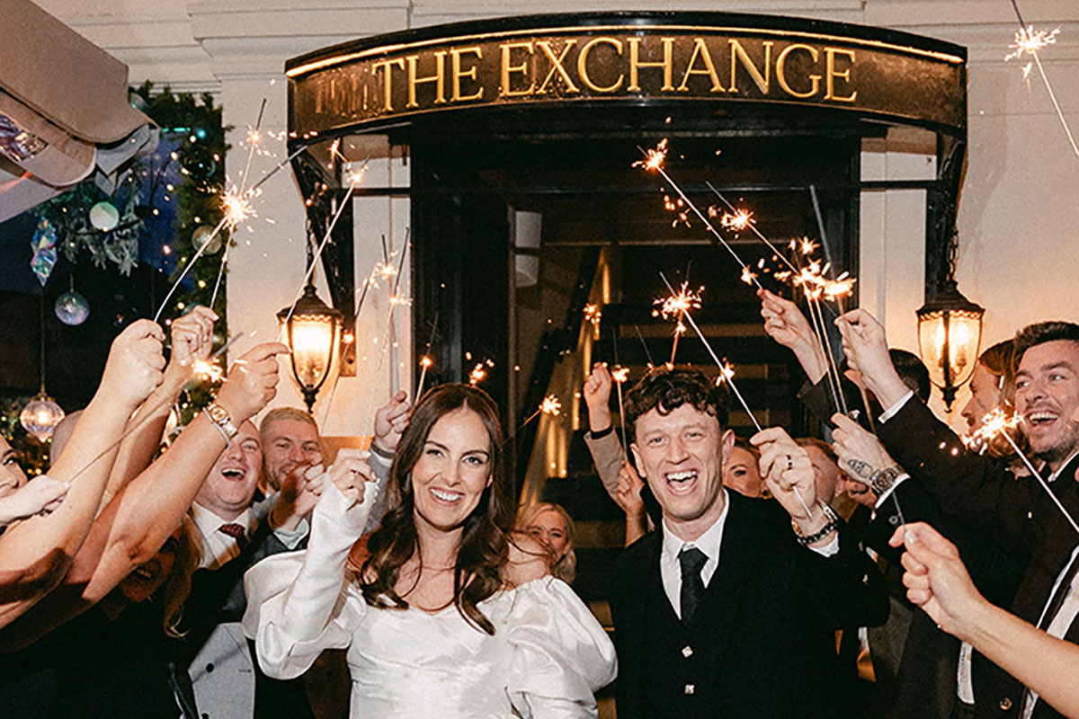bride and groom hold sparklers outside the exchange as wedding guests cheer them on