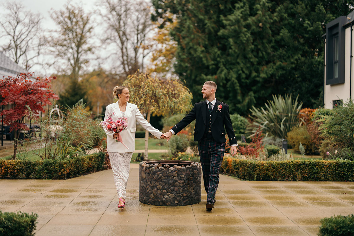 Bride and groom walk hand in hand through landscaped garden at Scottish wedding venue in autumn