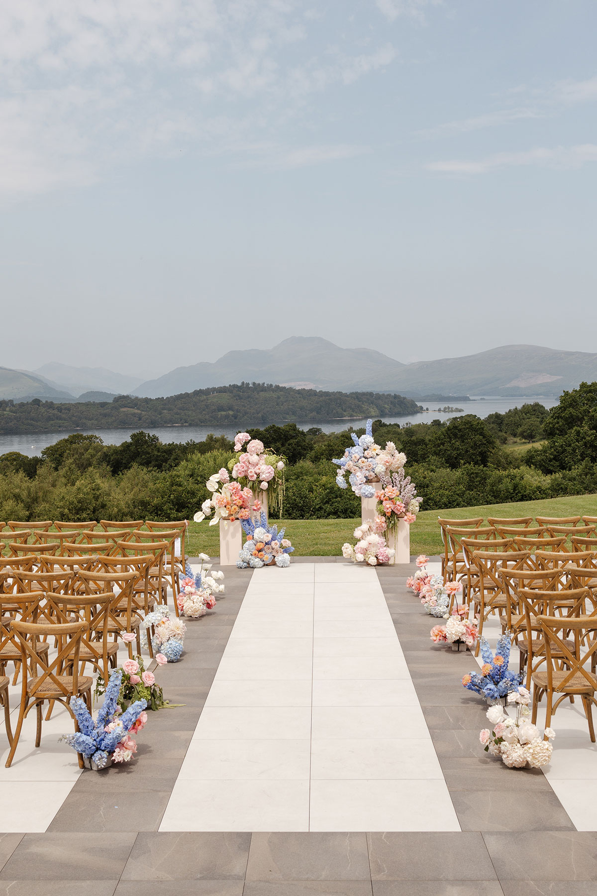 Outdoor wedding ceremony setup at Boturich Castle with colourful floral aisle arrangements and panoramic Loch Lomond views.