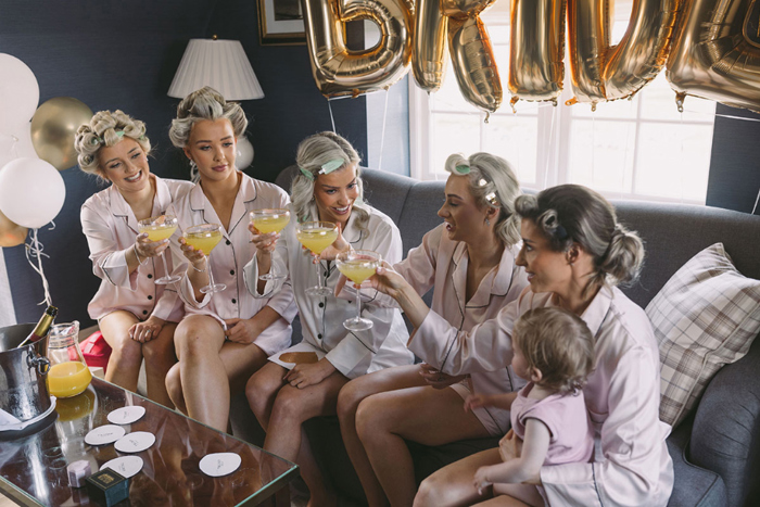 Bride and bridesmaids hold up glasses of orange juice while getting ready for the wedding