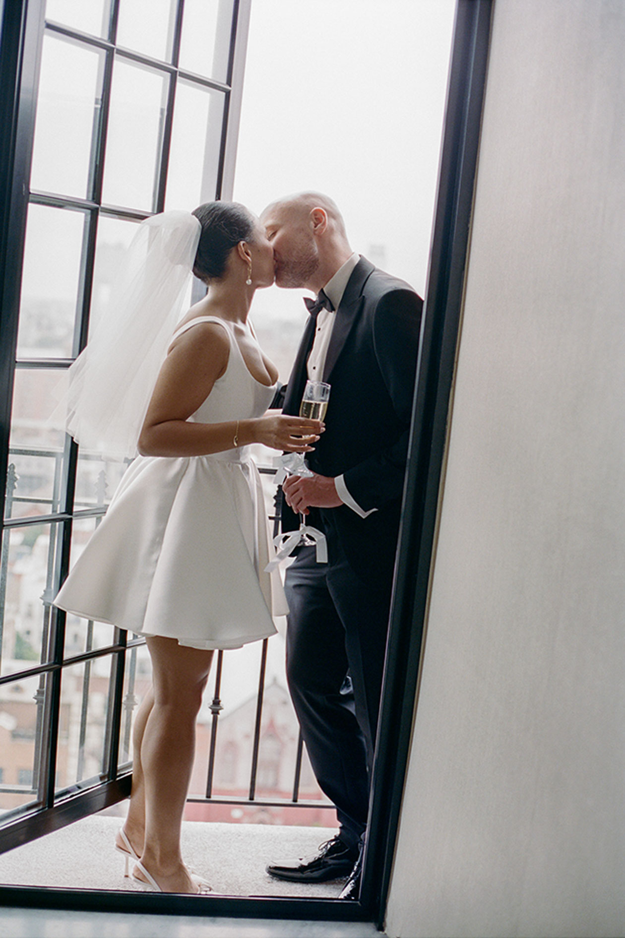 Bride and groom kissing on hotel balcony overlooking New York skyline with champagne