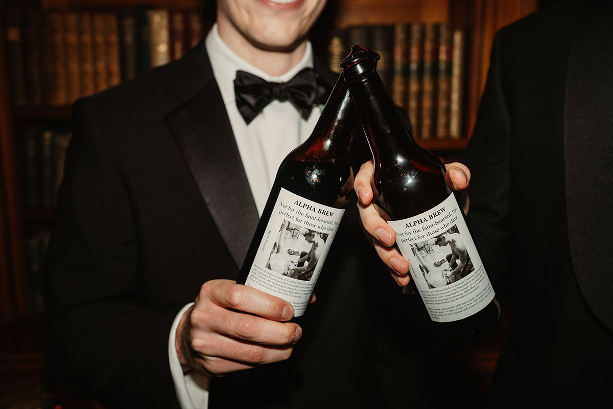 Two groomsmens’ hands holding personalised dark beer bottles with bespoke wedding labels.