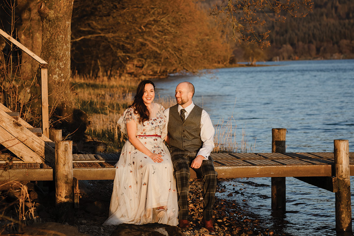 Bride and groom sitting on the dock by the loch at sunset
