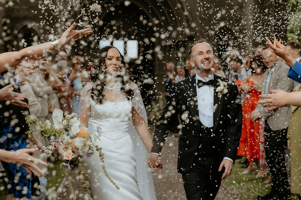 Bride and groom walking through confetti shower outside Rosebery House chapel, Midlothian wedding celebration.