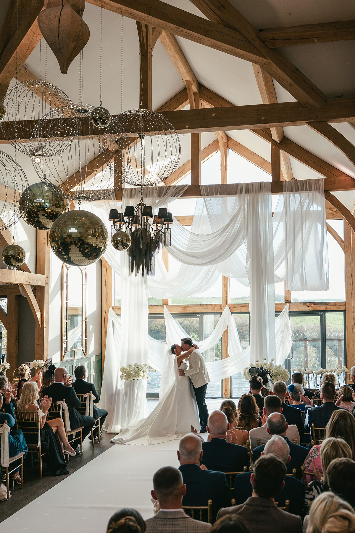 Newlyweds sharing first kiss during wedding ceremony in draped barn at Enterkine Country House