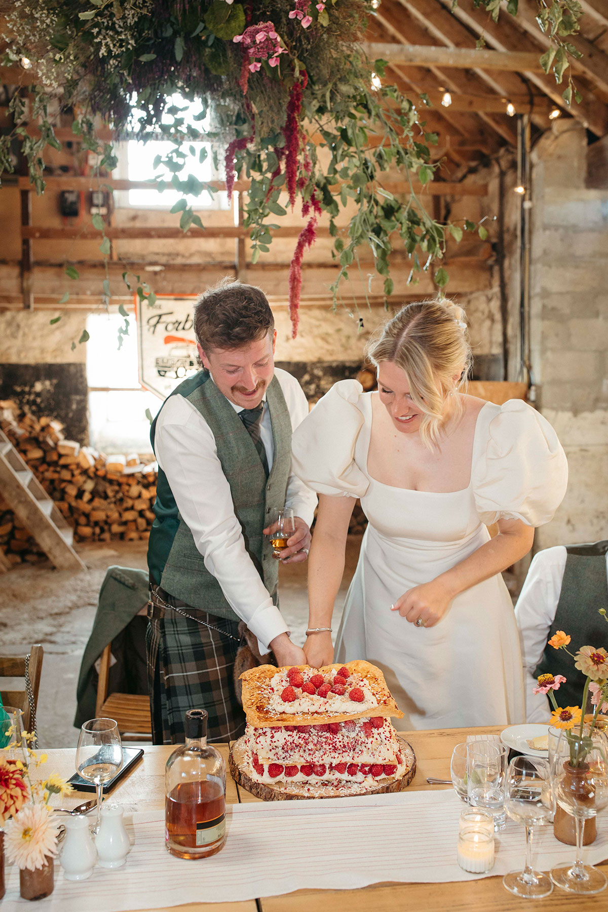 Bride and groom cut Scottish mille-feuille wedding cake inside rustic stone barn reception in the Cairngorms Highlands