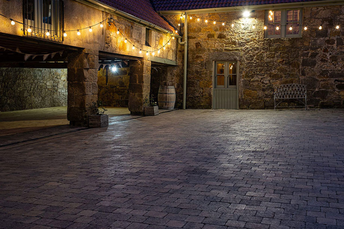 Evening courtyard at The Den at Culross, with warm festoon lighting illuminating the stone barns and cobbled ground