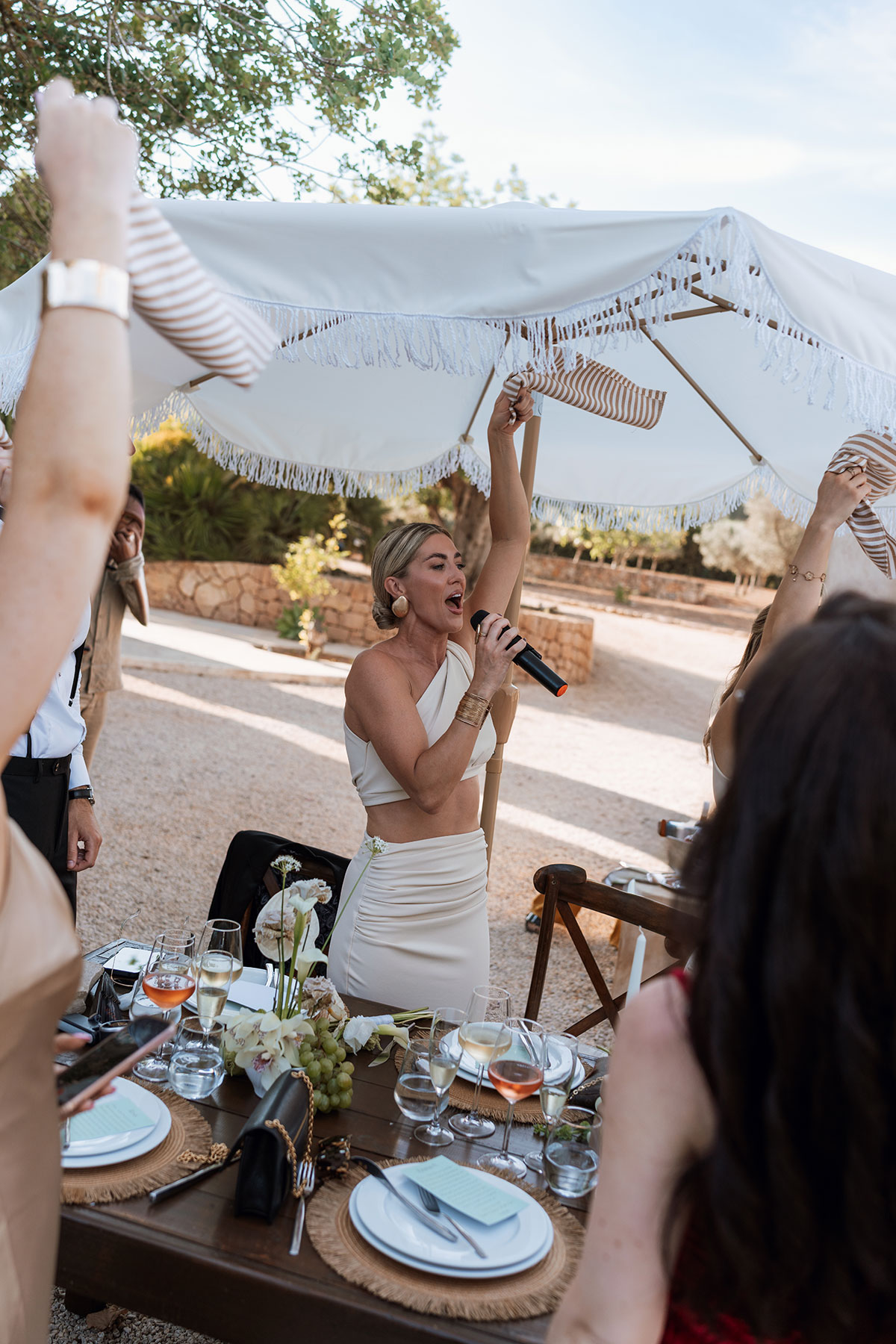 Bridesmaid giving speech and waving striped napkin during outdoor Ibiza wedding dinner celebration at Can Rafal