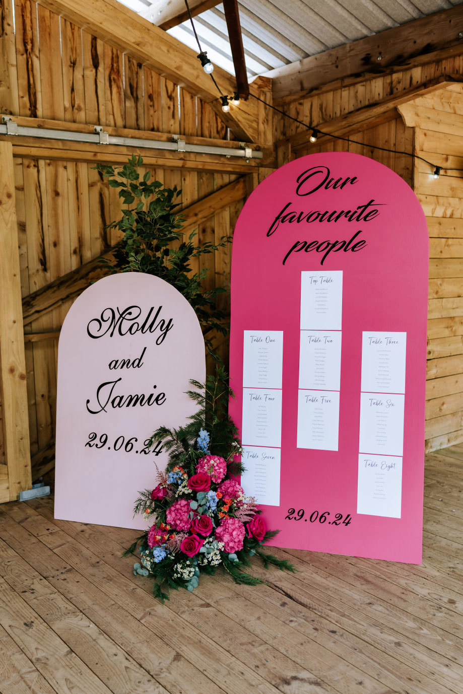 pink and red arched wedding signage in a wooden barn setting