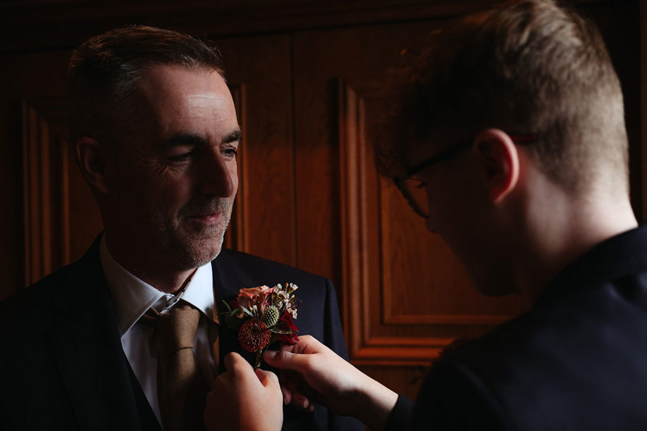 A man fixing a flower buttonhole onto another map's lapel 
