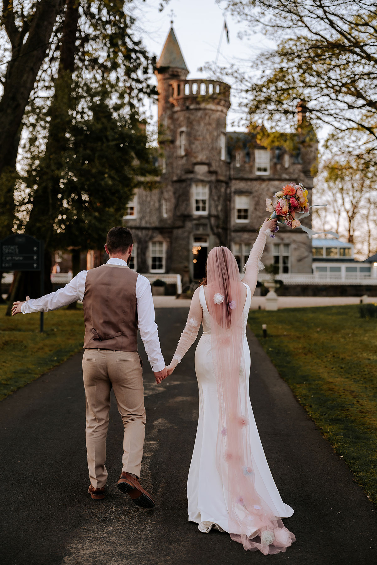 a bride and groom walking hand in hand towards Carlowrie Castle