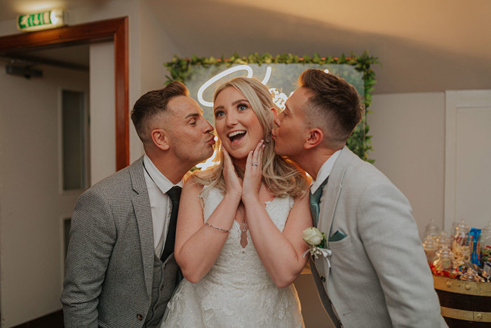 A Bride Being Kissed By Two Men Wearing Smart Grey Suits