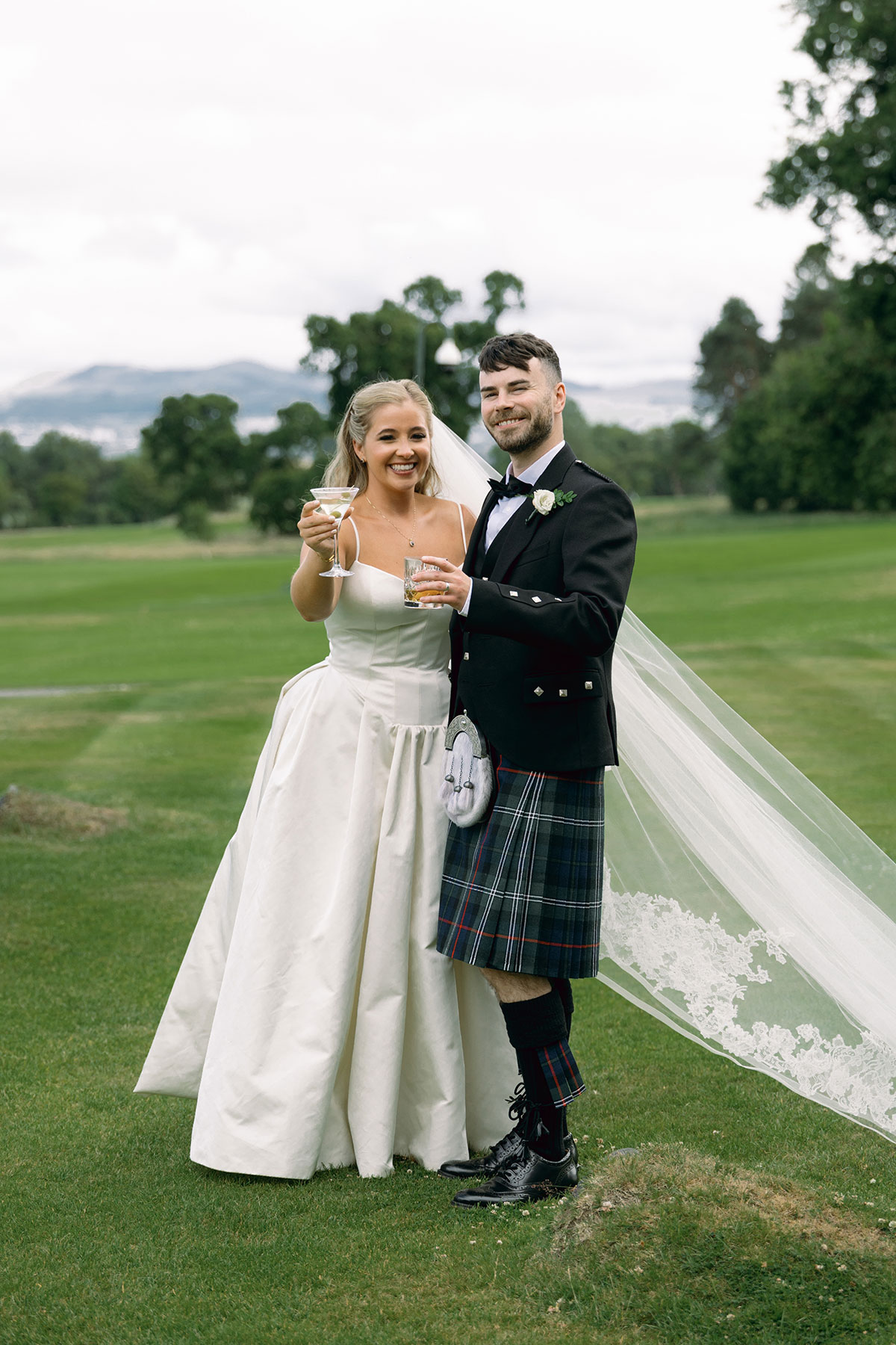 Bride and groom toast with cocktails on the lawn outside Dundas Castle during their Scottish destination wedding.
