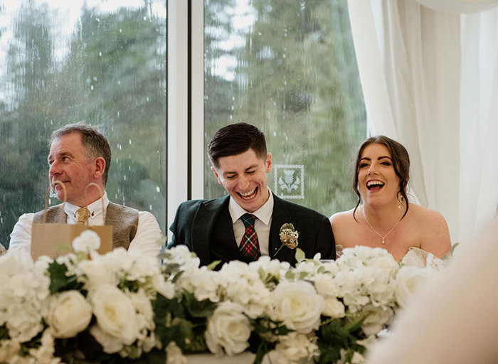 Two men and a woman laughing while sitting at a table with white flowers in front of them