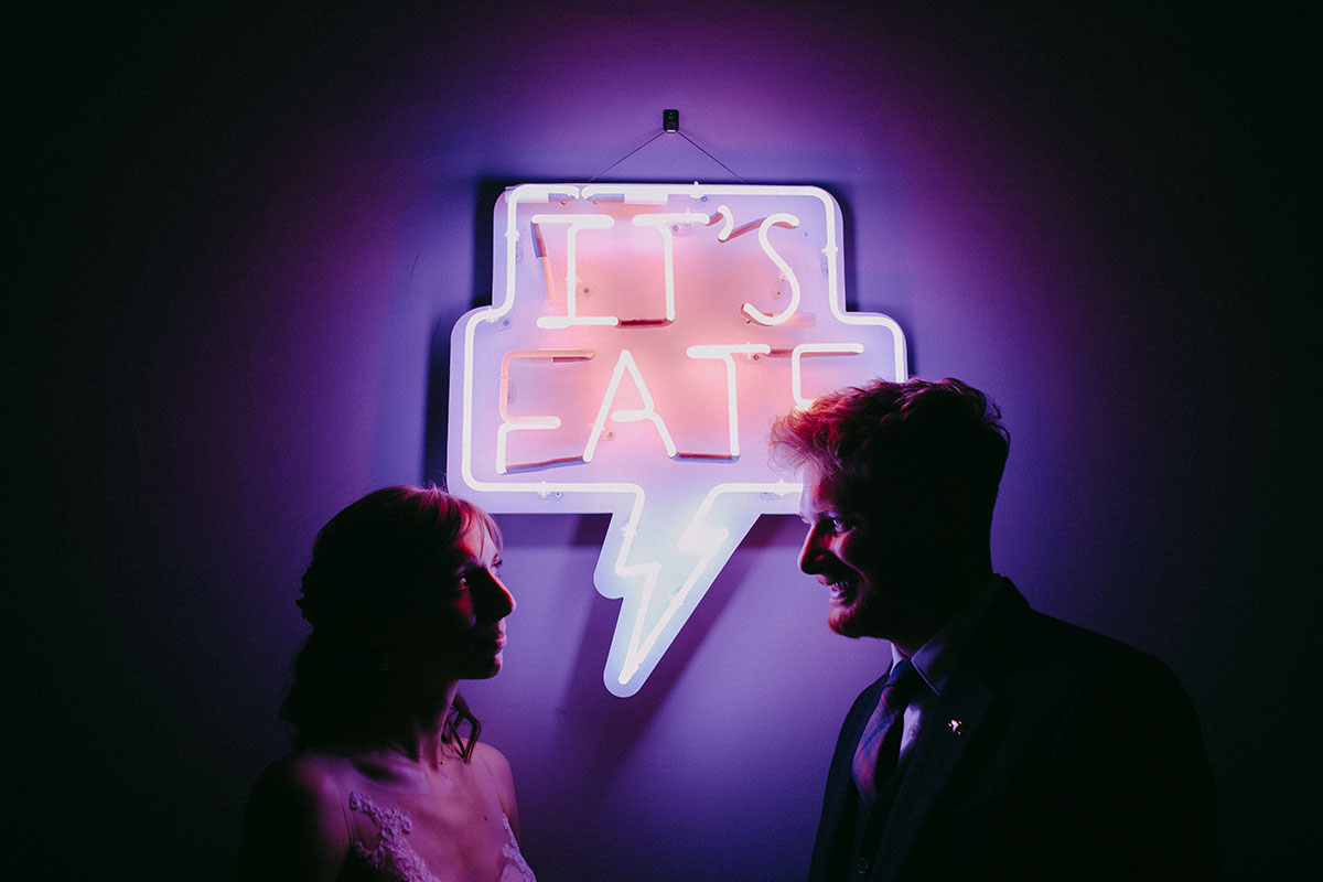 two people posing in front of a neon sign reading 'It's Fate'