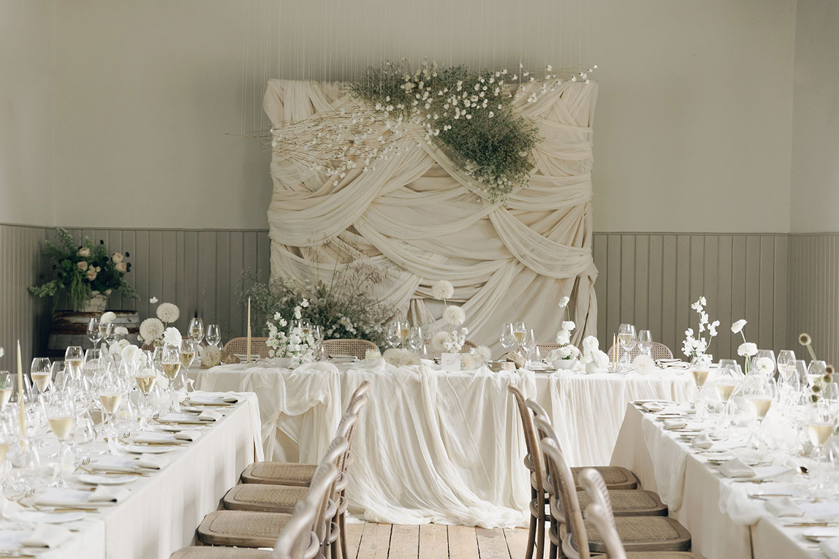 Wedding reception with draped fabric backdrop and neutral tablescape at Gilmerton House East Lothian