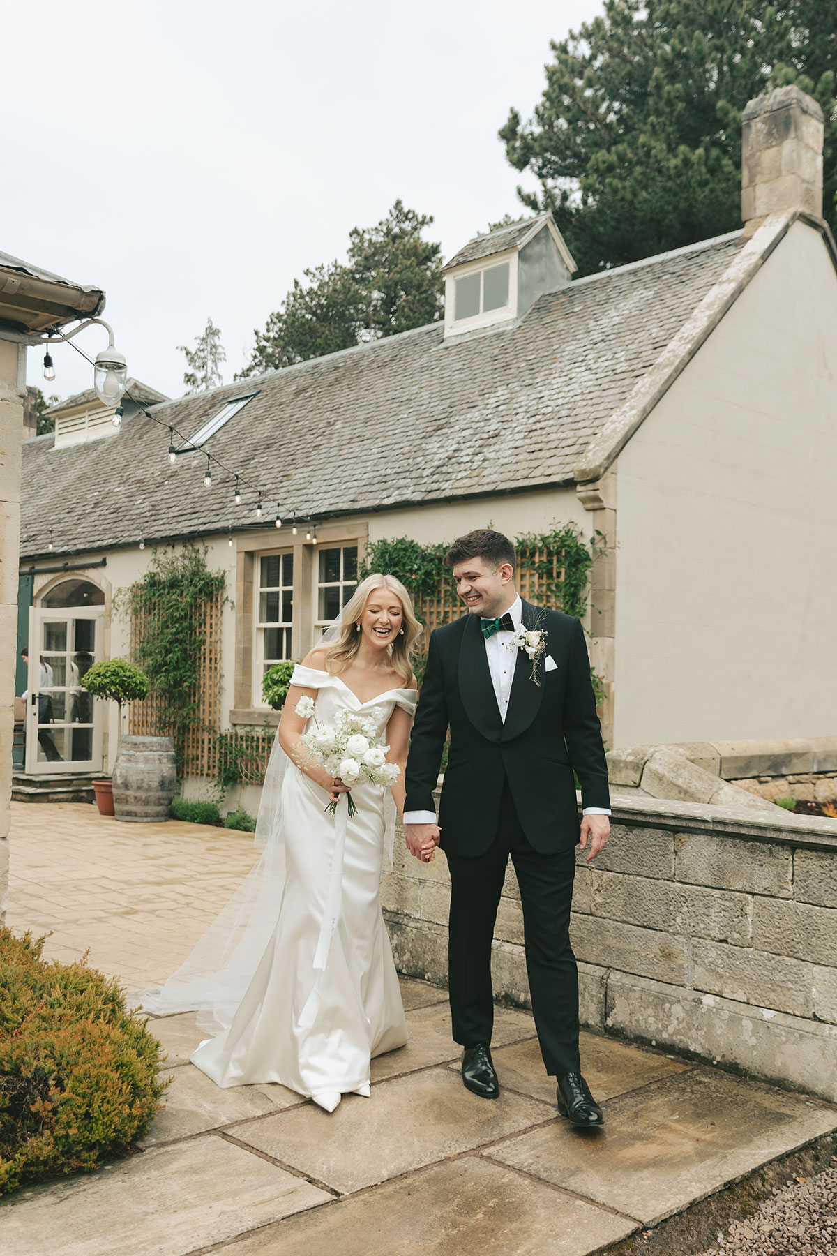 Bride and groom walking hand in hand outside Gilmerton House courtyard in East Lothian countryside