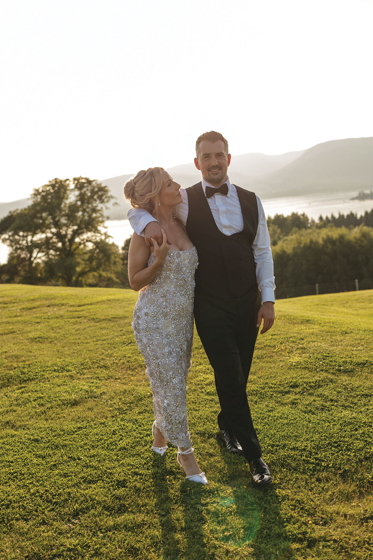 Bride and groom walk across the lawns at Boturich Castle during golden hour with Loch Lomond in the background.