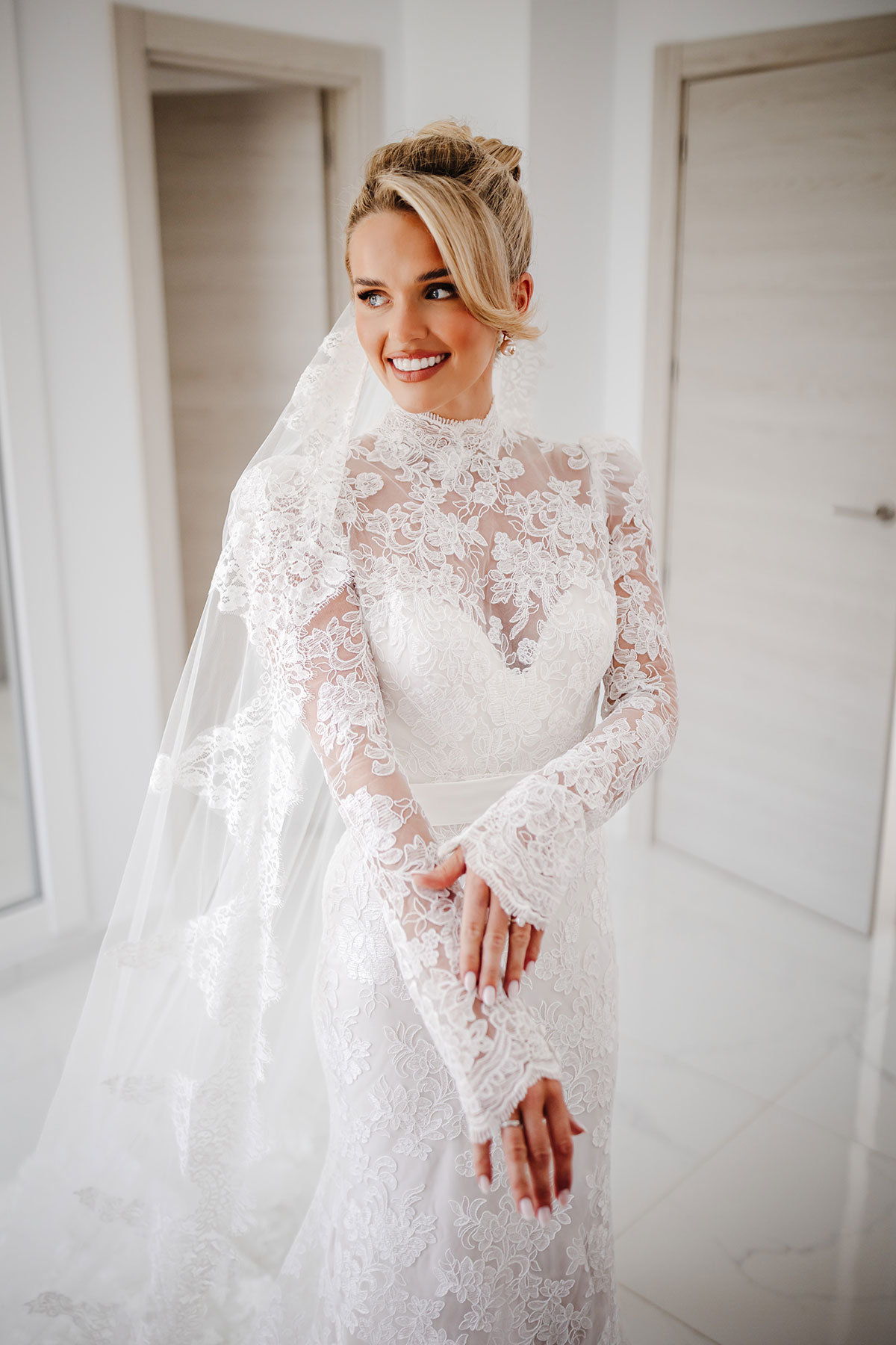 Bride in lace long-sleeve wedding dress smiles indoors before ceremony