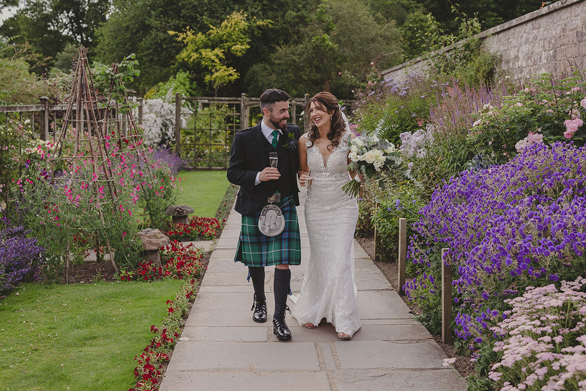 Newlyweds walking through the colourful walled gardens at Crathes Castle, surrounded by seasonal flowers and manicured borders