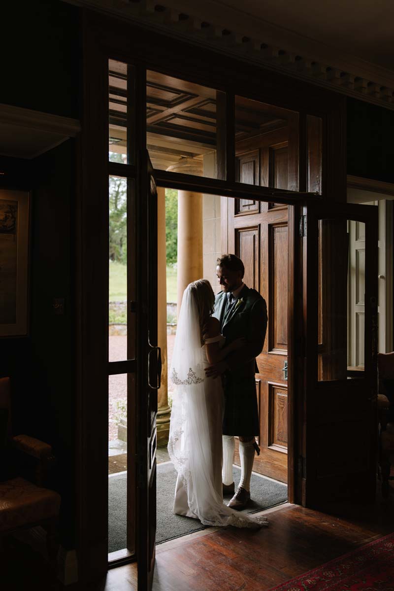 Lia and Louis share a quiet moment in the doorway at Cambo House during their Fife wedding.