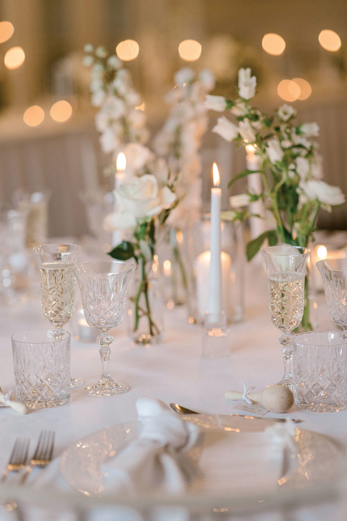 white tablescape with clear crystal glassware, white candlesticks, and green and white bud vases
