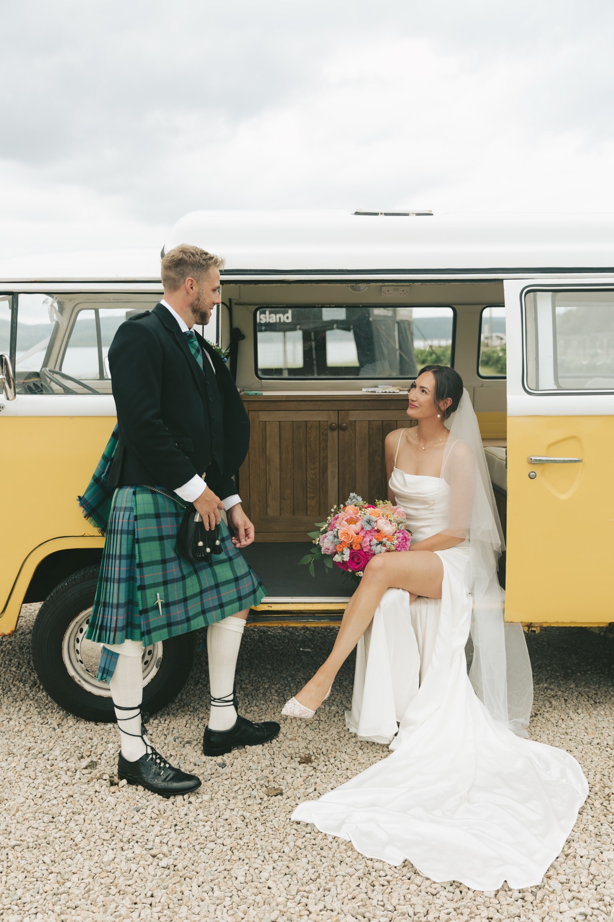 Isobel and Gary pose beside a yellow vintage VW campervan at their coastal wedding at The Dougarie Boathouse.