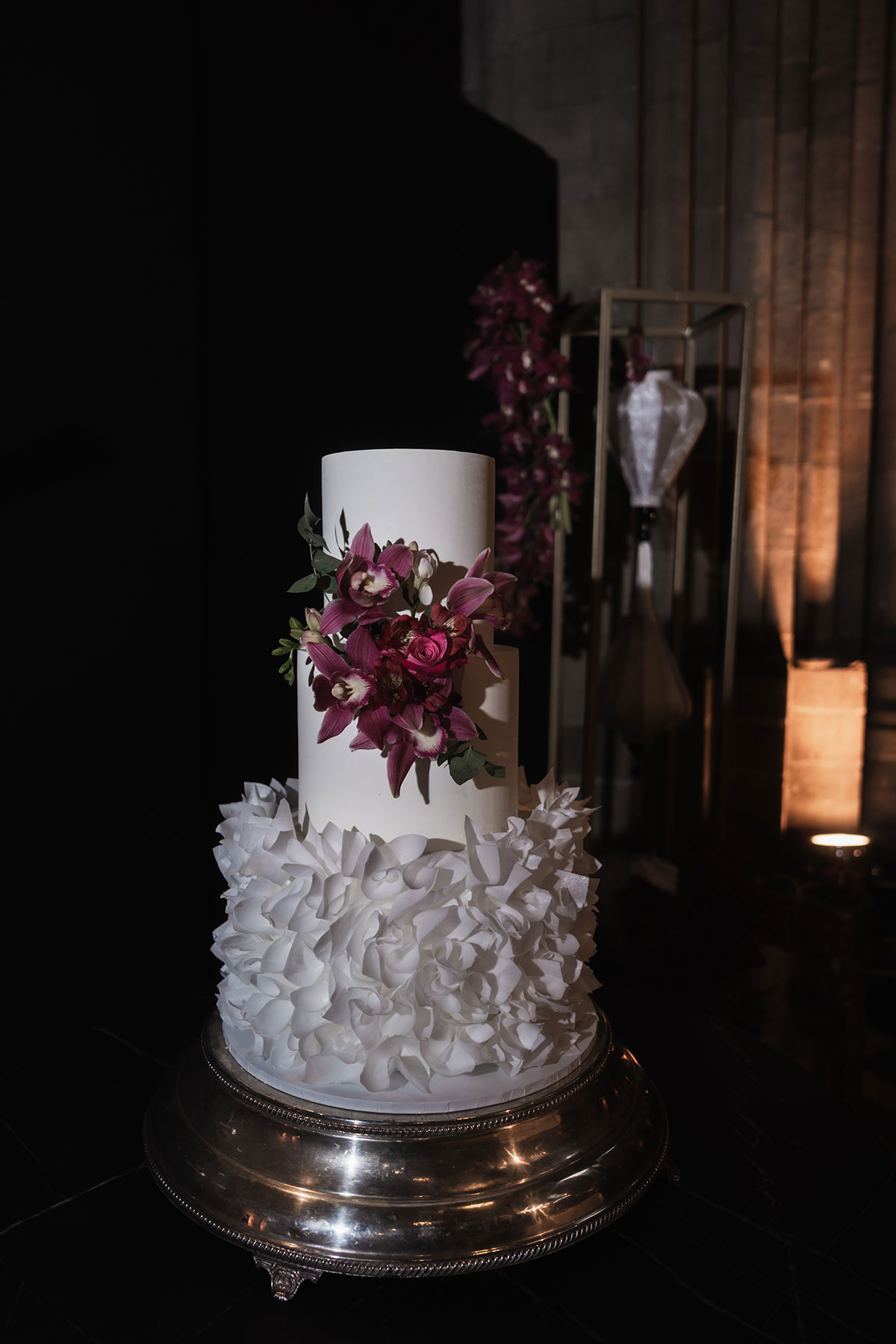 Close-up of white ruffled wedding cake with cascading pink orchids at Mansfield Traquair