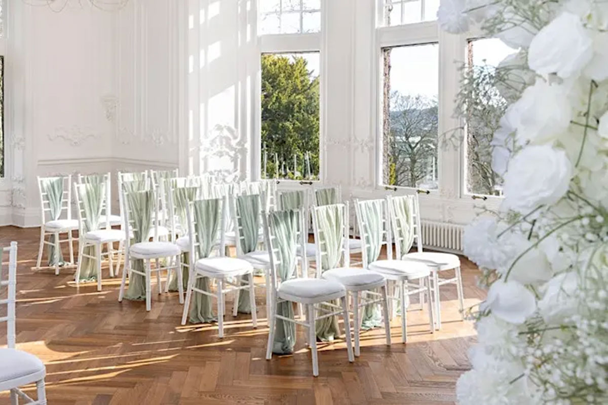 rows of white Chiavari white chairs with pale green sashes are lined up for a wedding ceremony