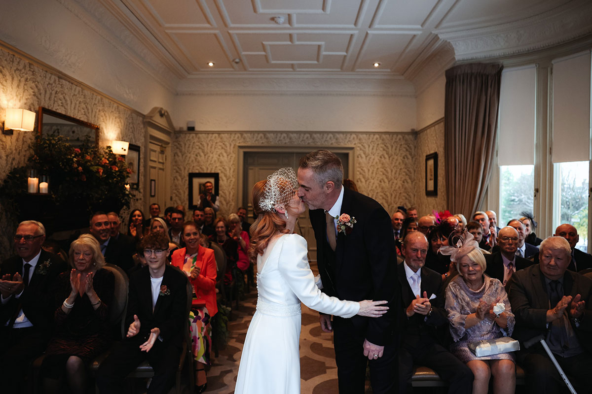 A bride and groom kiss in front of their seated guests