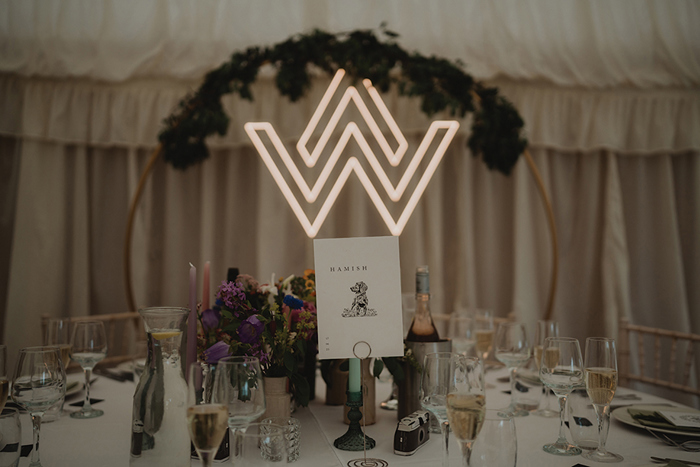 A Wedding Table Dressed For Dinner With Illuminated Sign In Background