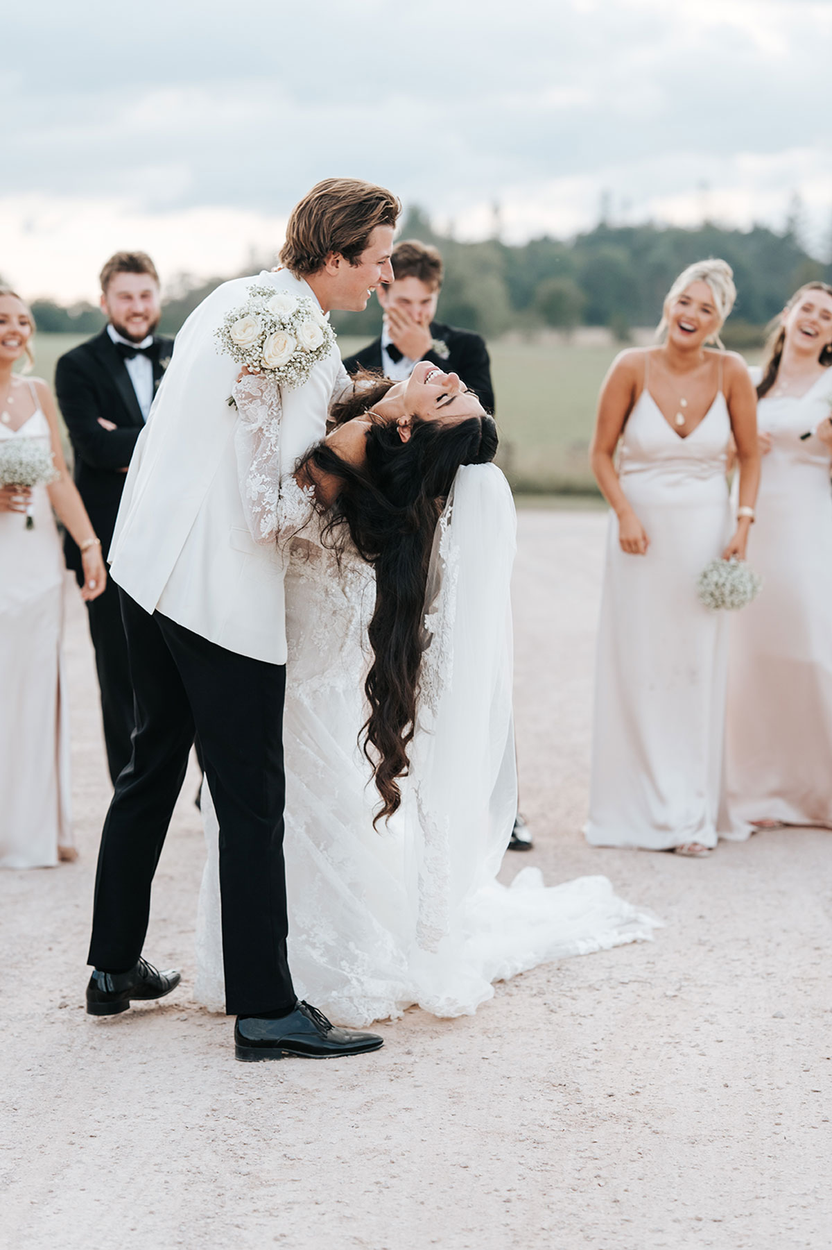 Groom dipping the bride during wedding portraits as the bridal party laughs in the background