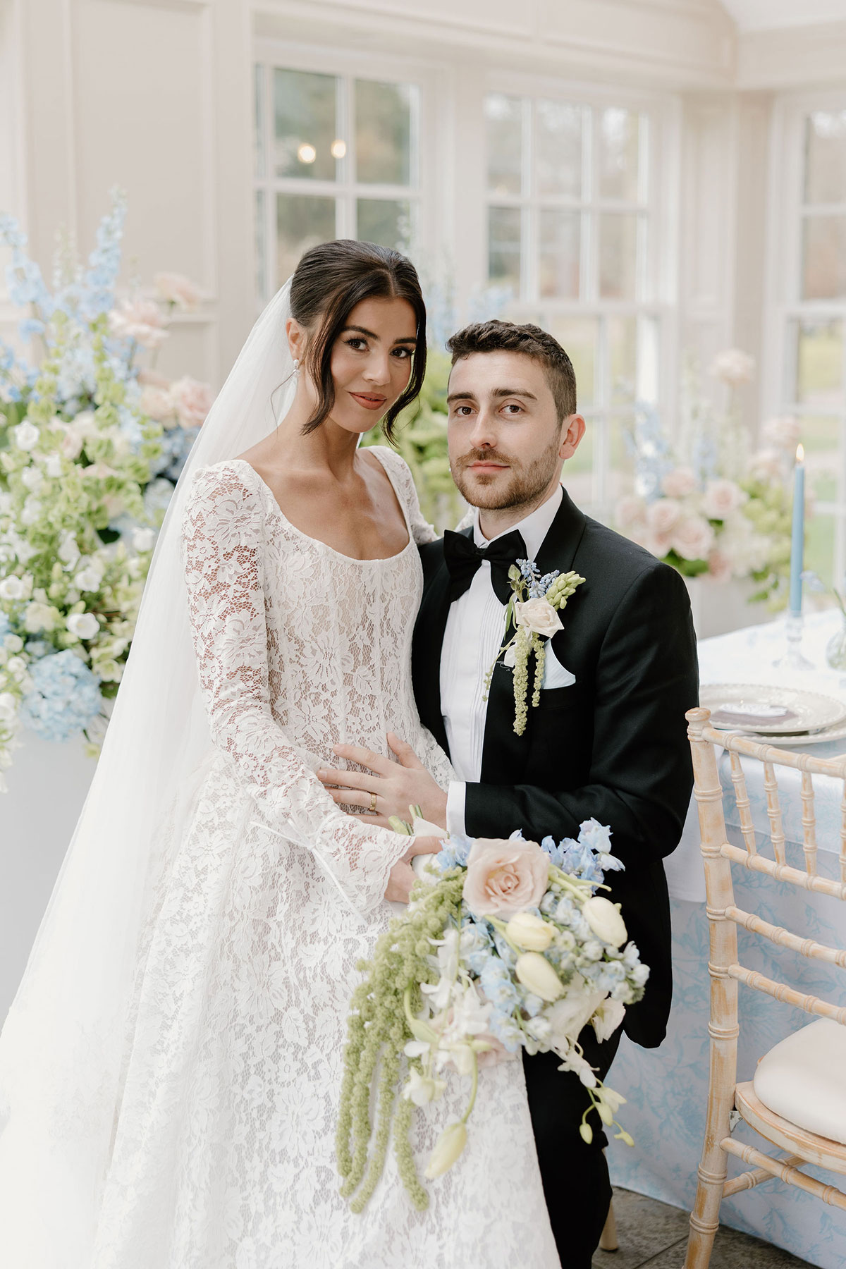 Bride and groom posing beside a floral reception table with a bouquet in the foreground