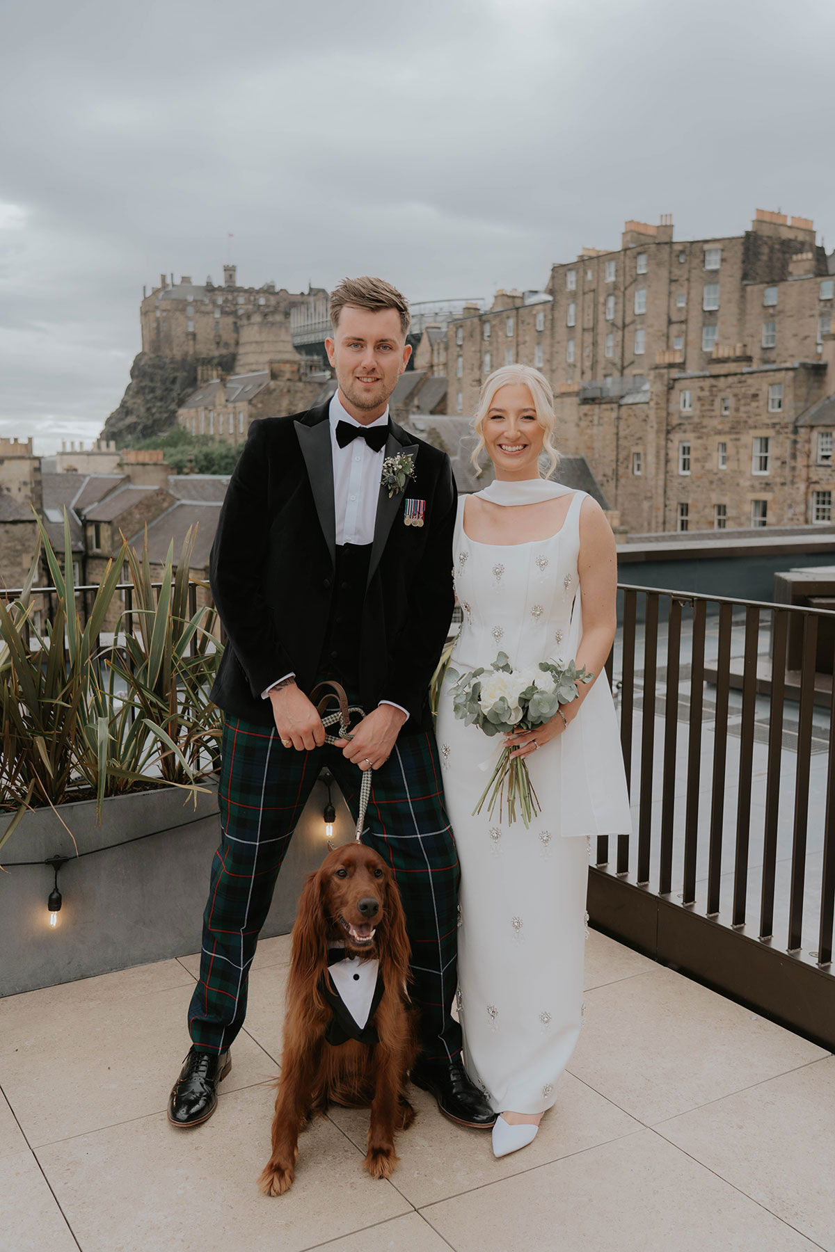 Bride and groom with their red setter on a rooftop overlooking Edinburgh Castle after their city wedding