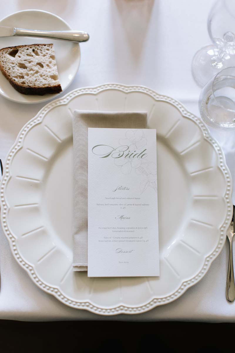 Wedding breakfast place setting at Cambo House with a personalised bride menu on a white scalloped plate.