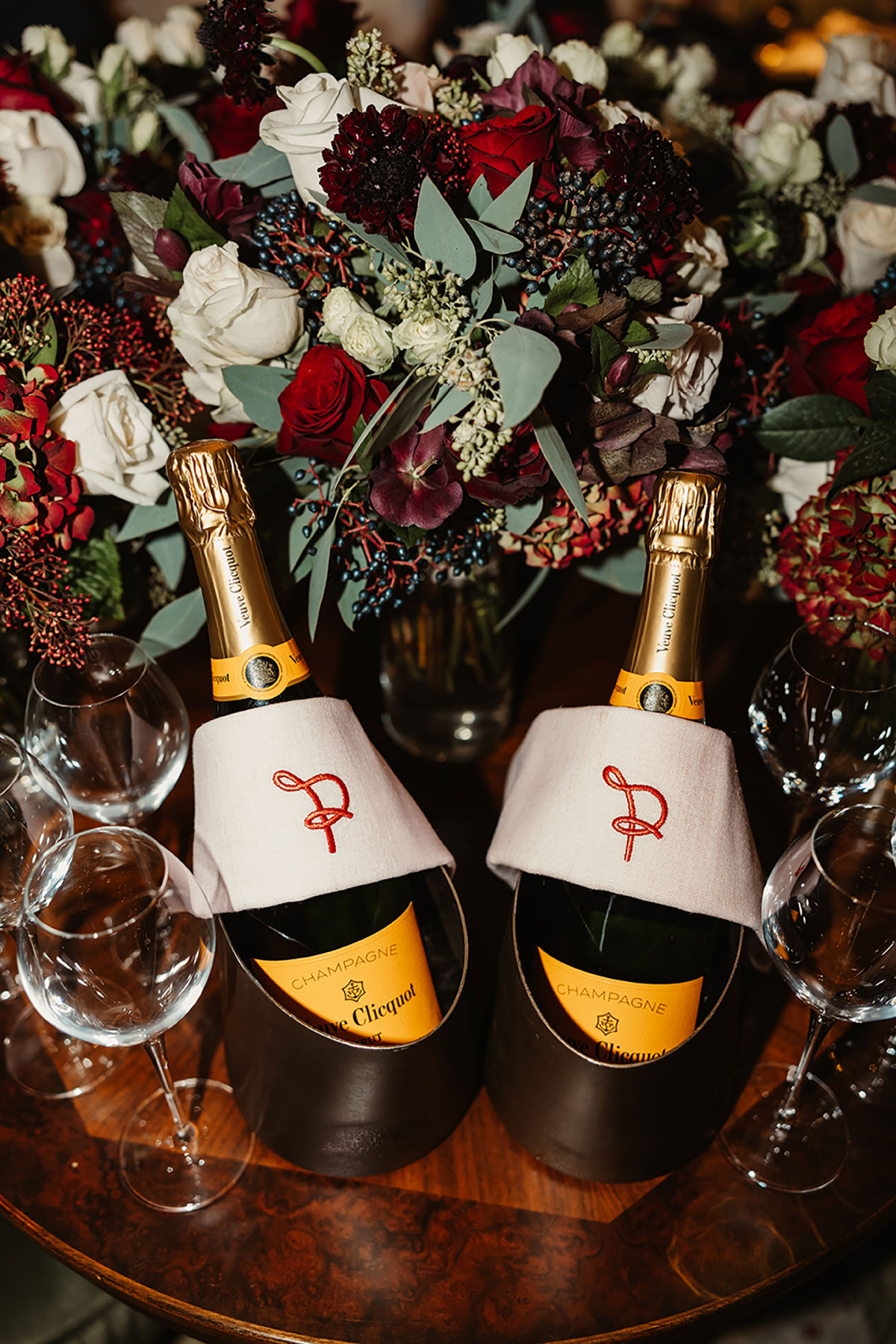 Two bottles of Veuve Clicquot in embroidered coolers surrounded by rich red, white and burgundy winter florals.