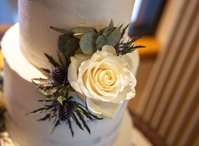 A close up of a wedding cake with white icing and a white rose decoration 