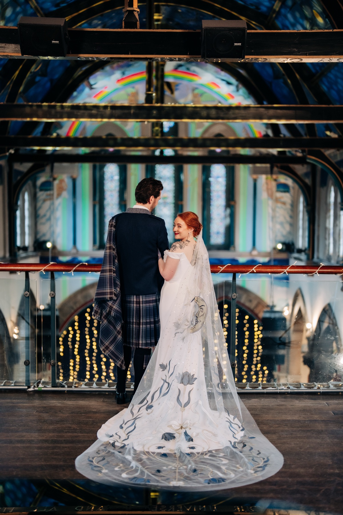Newlyweds Robyn and James pose on the balcony at Òran Mór in Glasgow, showing Robyn’s bespoke moon-and-stars wedding veil.