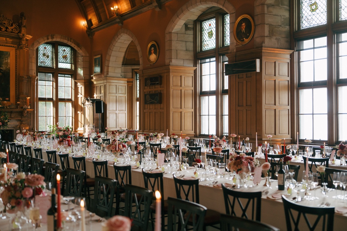 Long wedding reception tables at Barnbougle Castle decorated with pink-and-red floral centrepieces, candles and personalised place settings.
