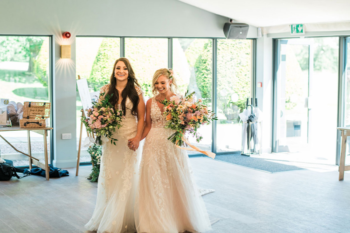 Two brides carrying bouquets enter wedding reception